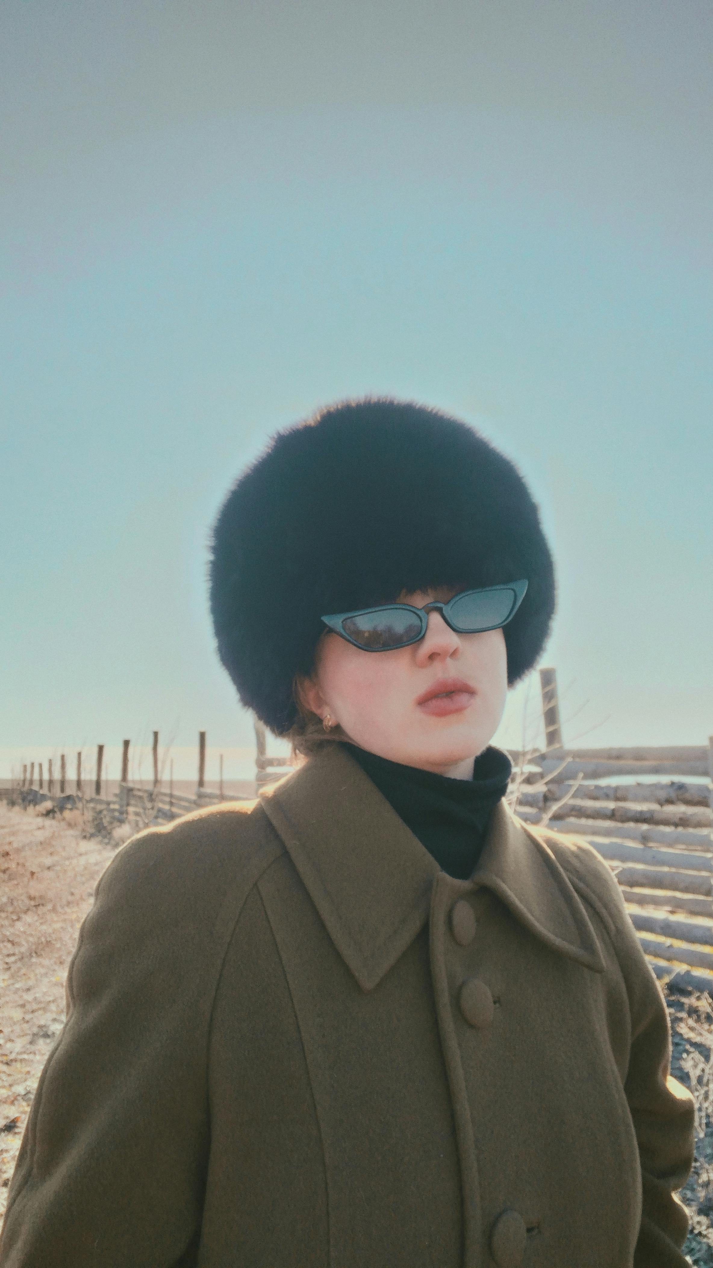 Fashionable woman in fur hat and sunglasses outdoors against a winter backdrop.
