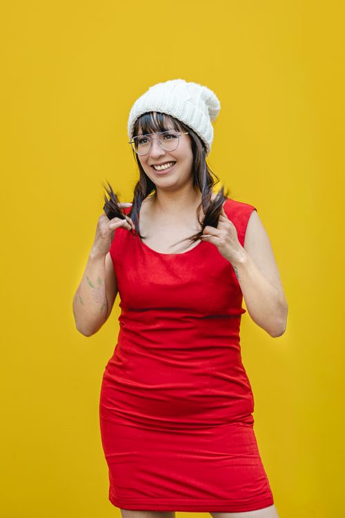 Free Smiling woman in red dress and white beanie against vibrant yellow background. Stock Photo