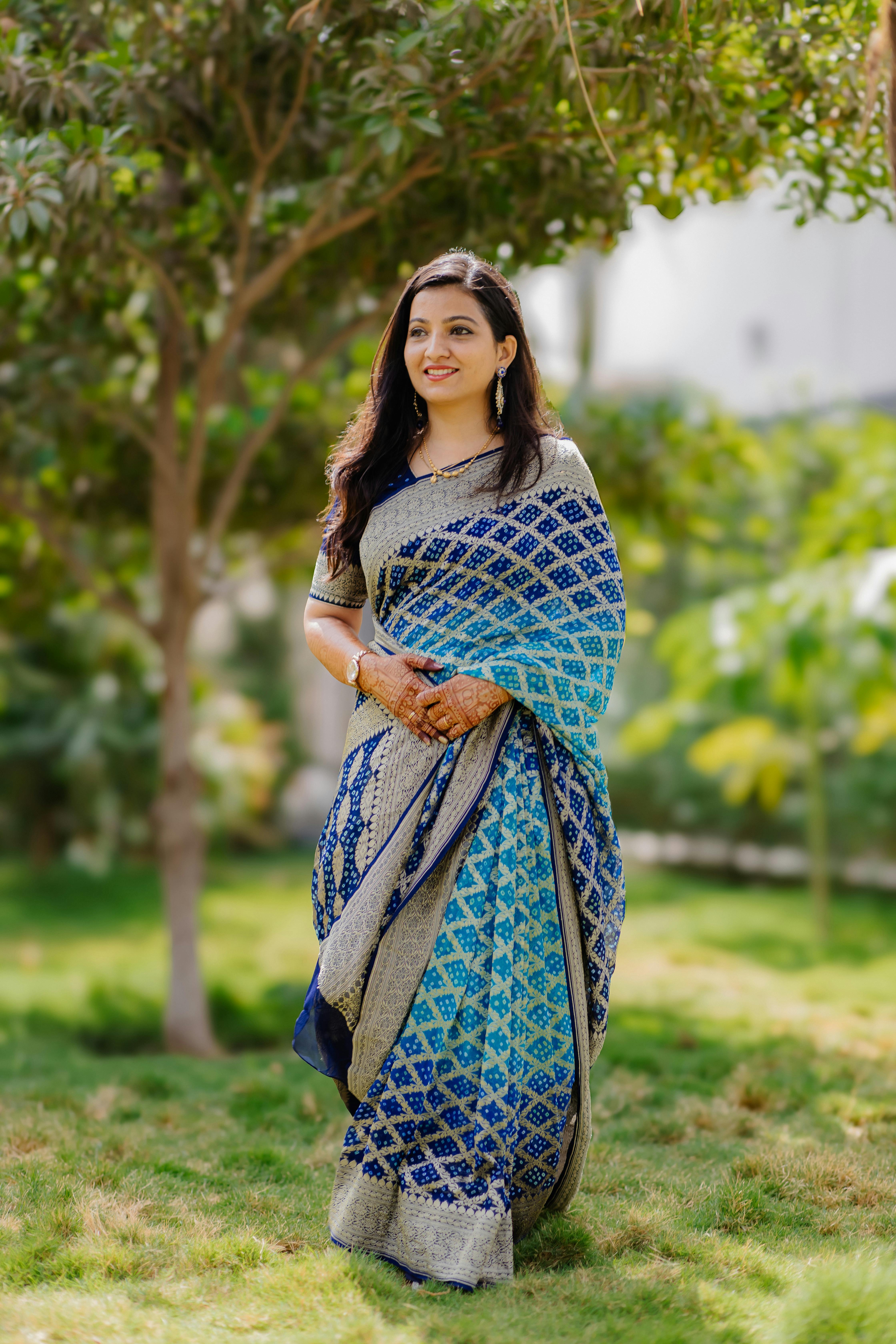 Gratis Una mujer sonriente con un sari estampado de color azul se encuentra de pie con gracia al aire libre en un jardín. Foto de stock