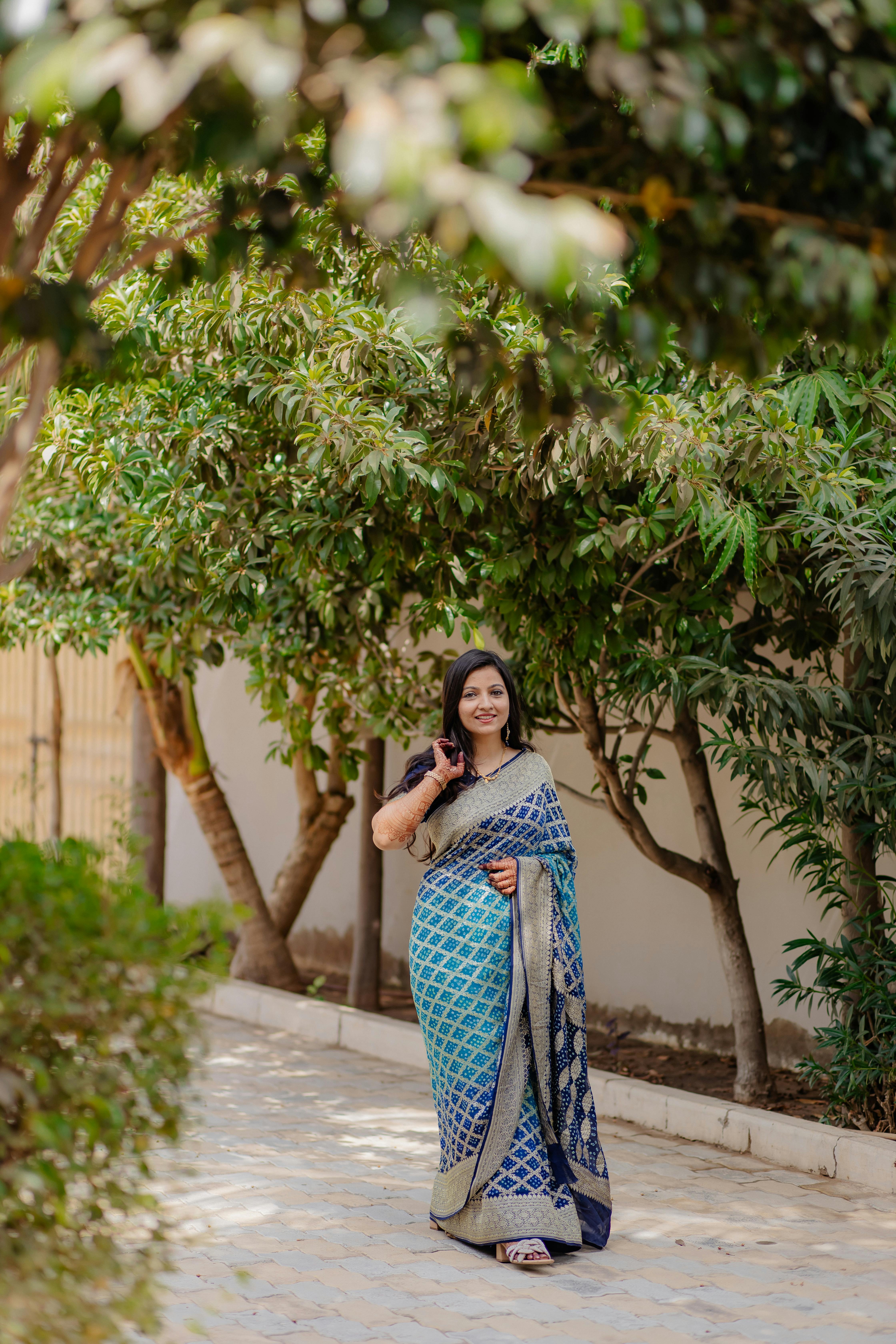 De franc Una dona amb un preciós sari blau camina tranquil·lament per un camí vorejat d'arbres a l'aire lliure. Foto d'estoc