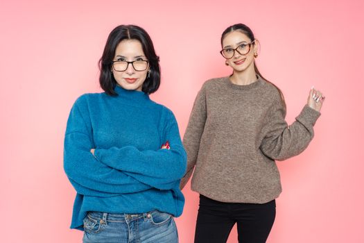 Two smiling women posing in casual sweaters against a vibrant pink backdrop.