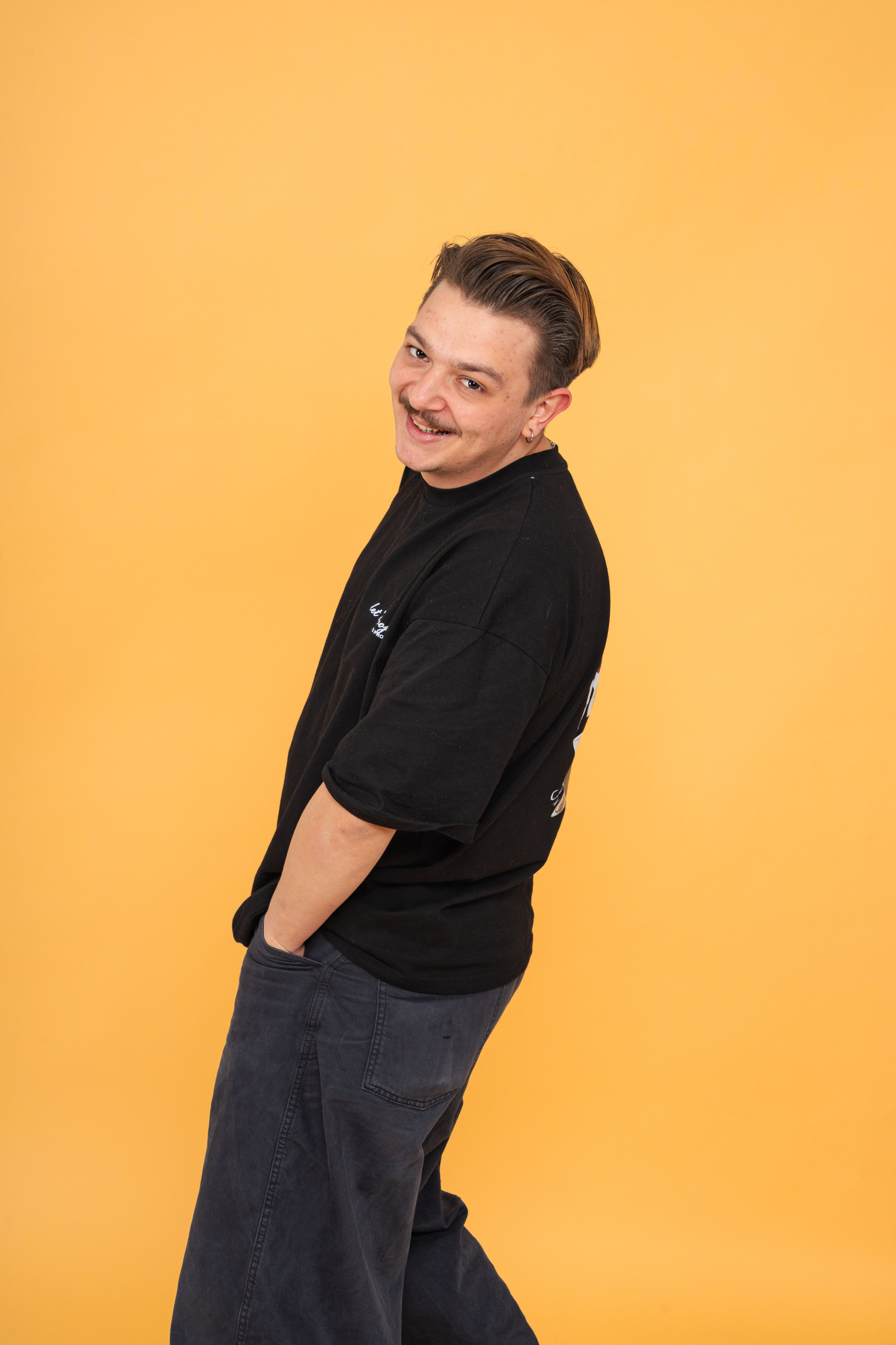 Friendly adult smiling in black shirt against a yellow studio backdrop.