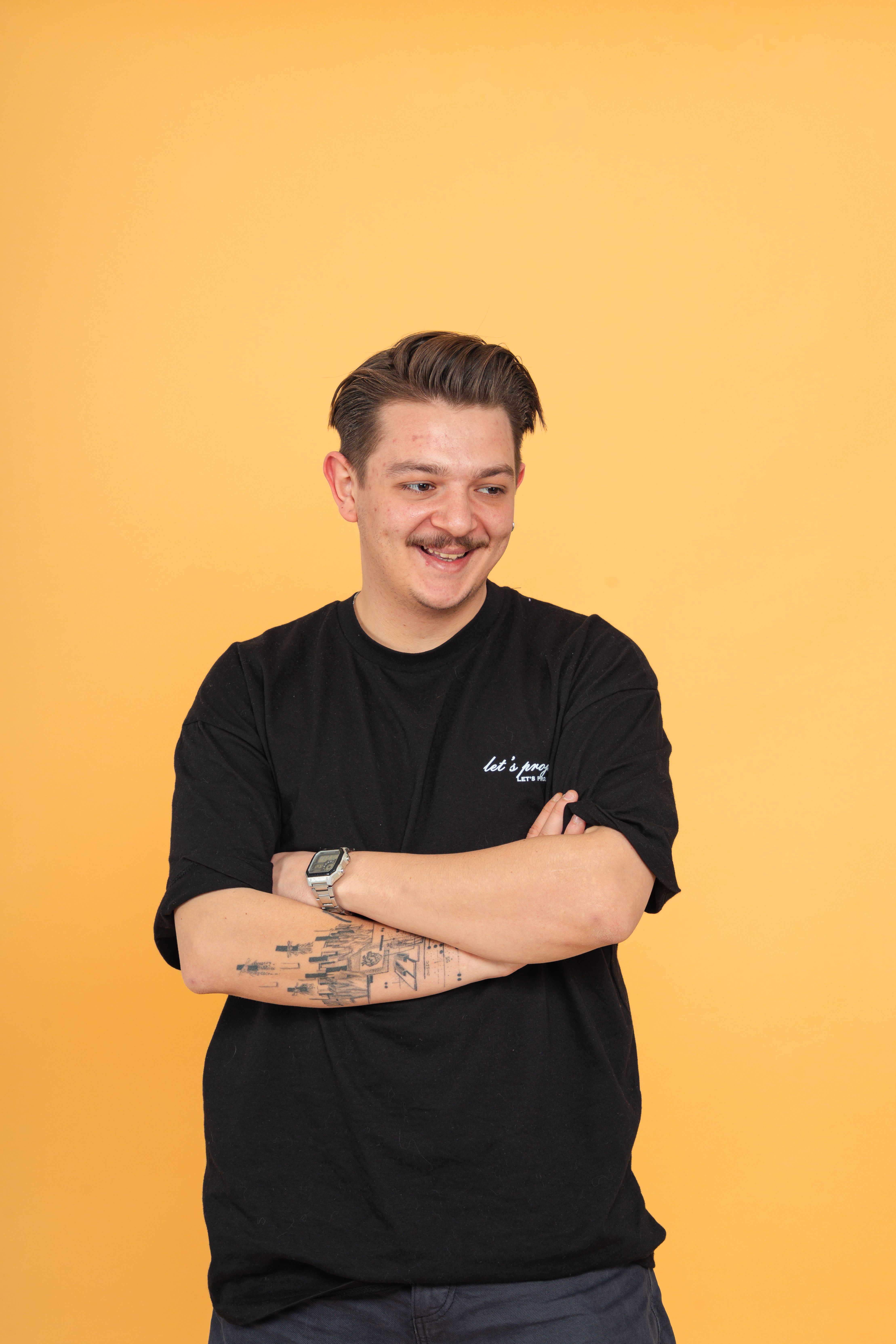 Confident smiling man with tattoos stands against a bright yellow backdrop.