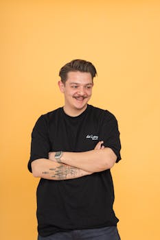 Confident smiling man with tattoos stands against a bright yellow backdrop.