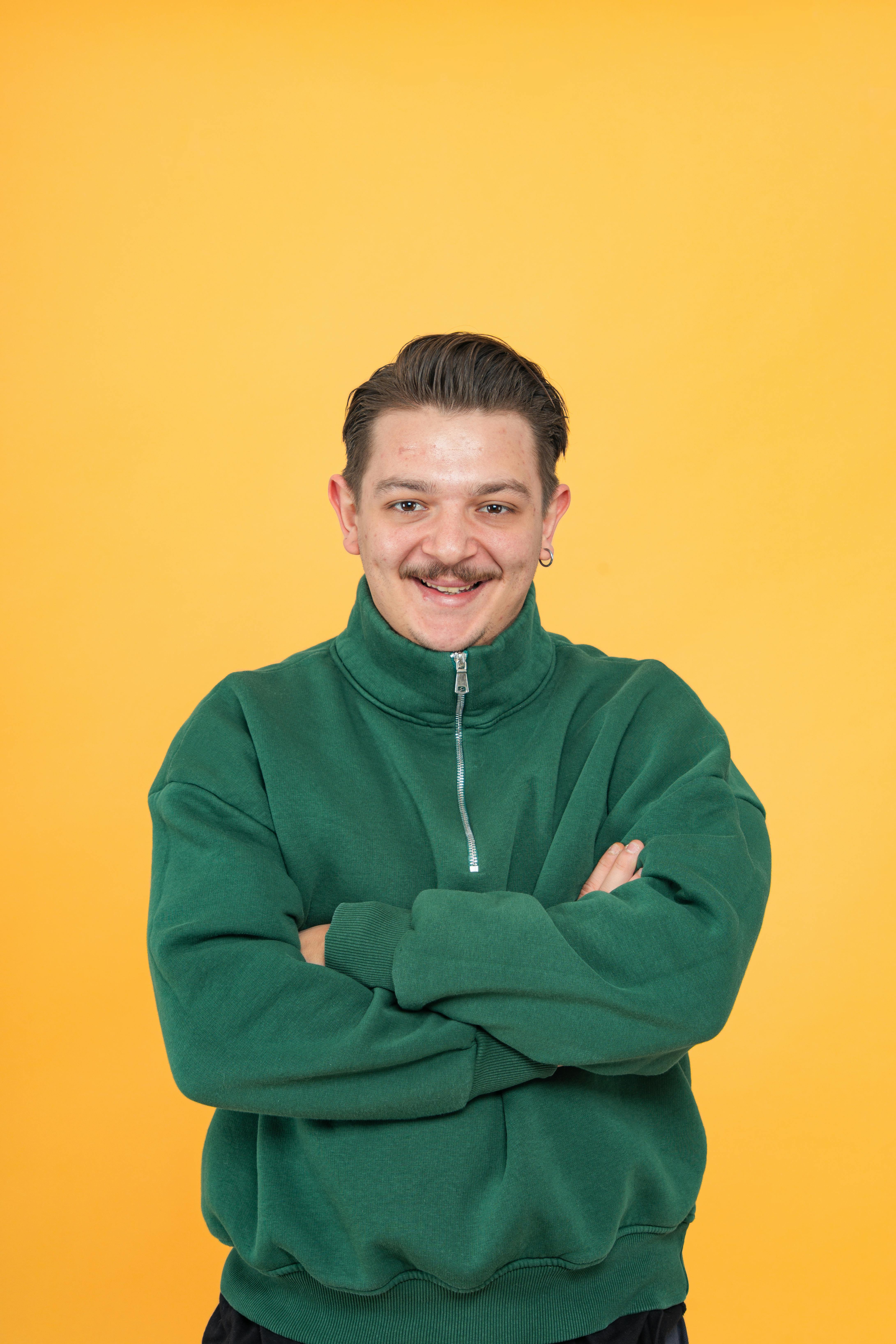 Miễn phí Chân dung một người đàn ông đang mỉm cười trong chiếc áo len màu xanh lá cây, nổi bật trên nền màu vàng rực rỡ. Ảnh lưu trữ