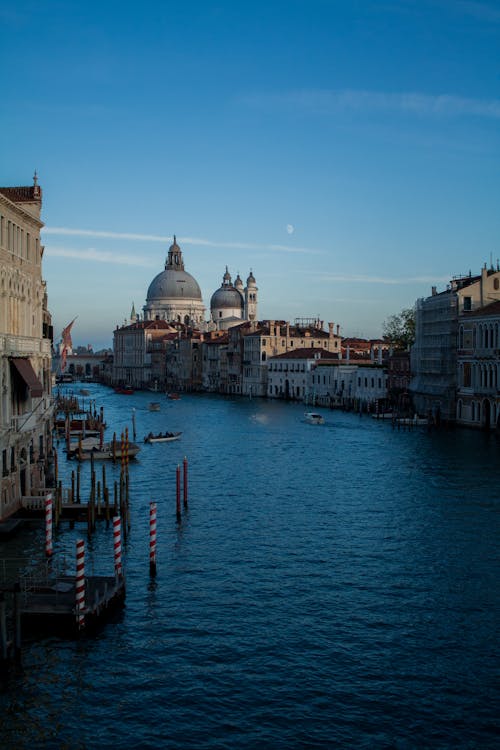 Blue canal water flowing among old city buildings and domed church located in Venice
