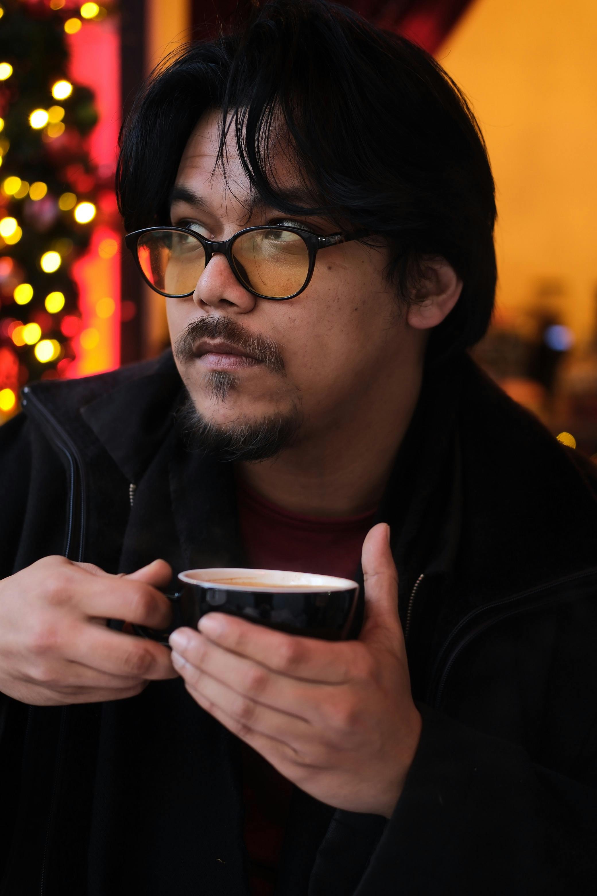 Gratis Hombre con gafas saboreando una bebida caliente en el interior durante la temporada navideña. Foto de stock