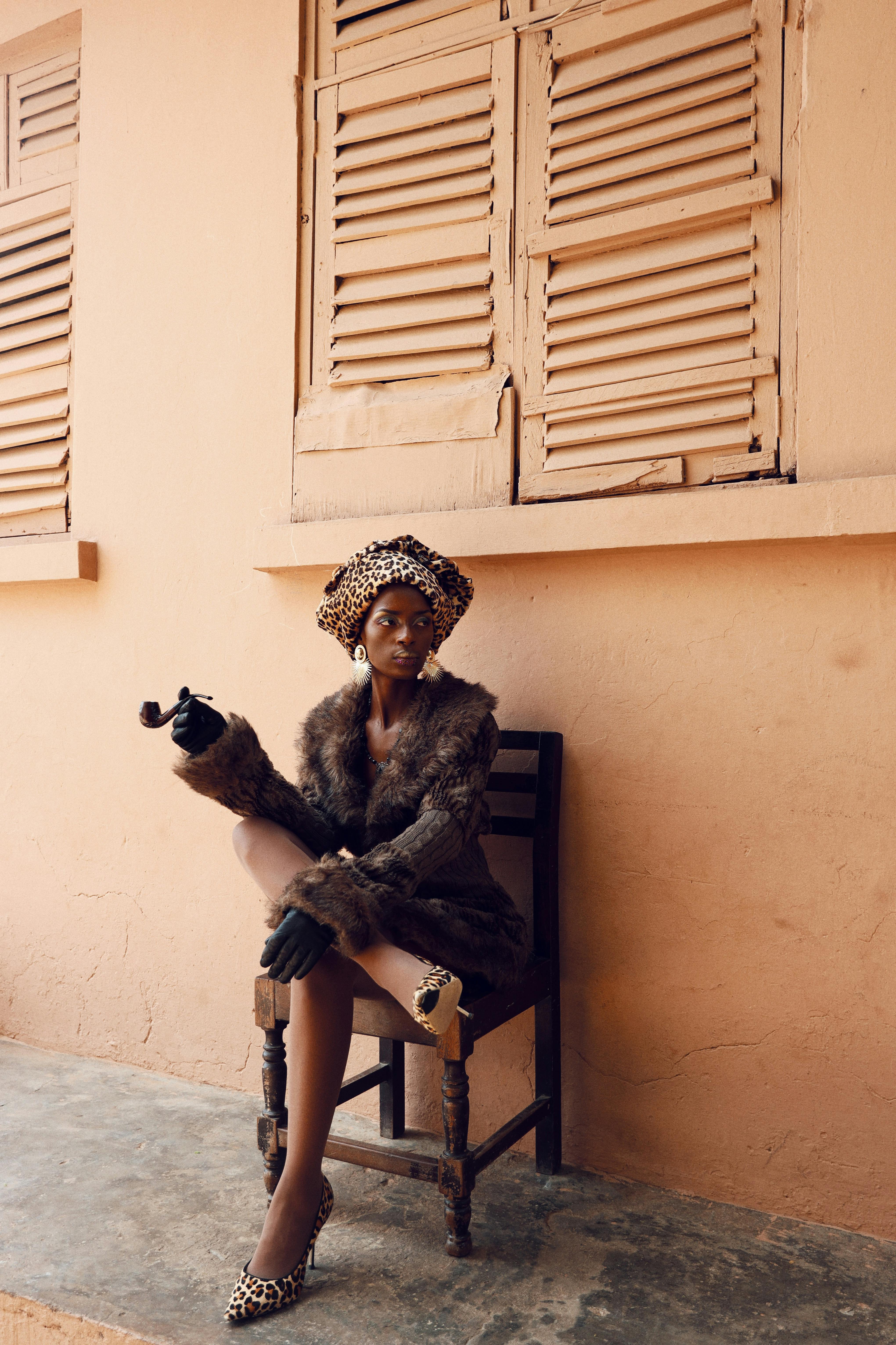 Kostenlos Eine elegante Frau in Leopardenmuster-Kleidung sitzt vor einem pastellfarbenen Gebäude und strahlt modernen Stil und Selbstbewusstsein aus. Stock-Foto