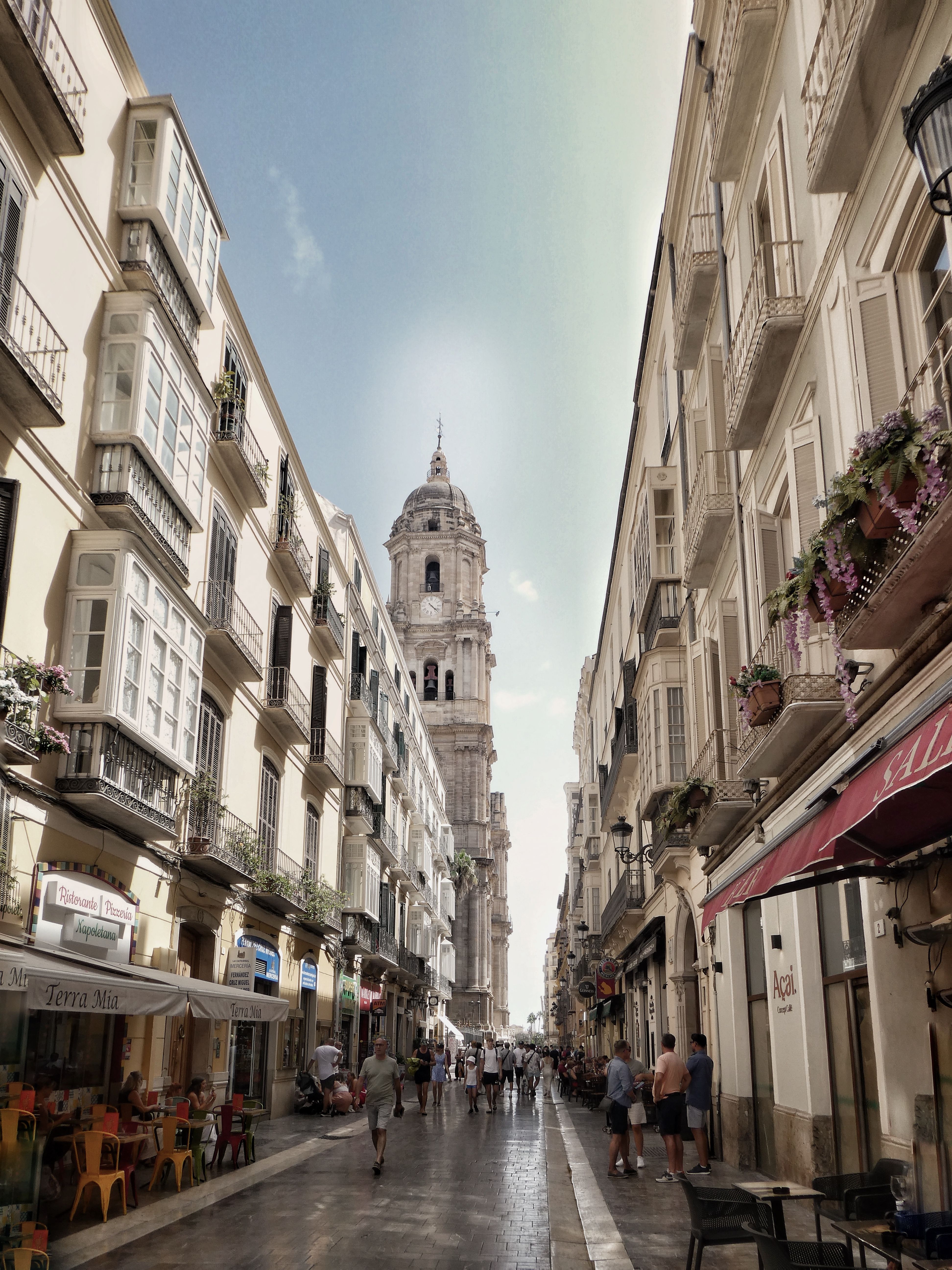 People stroll down a picturesque street in Málaga with Cathedral backdrop.