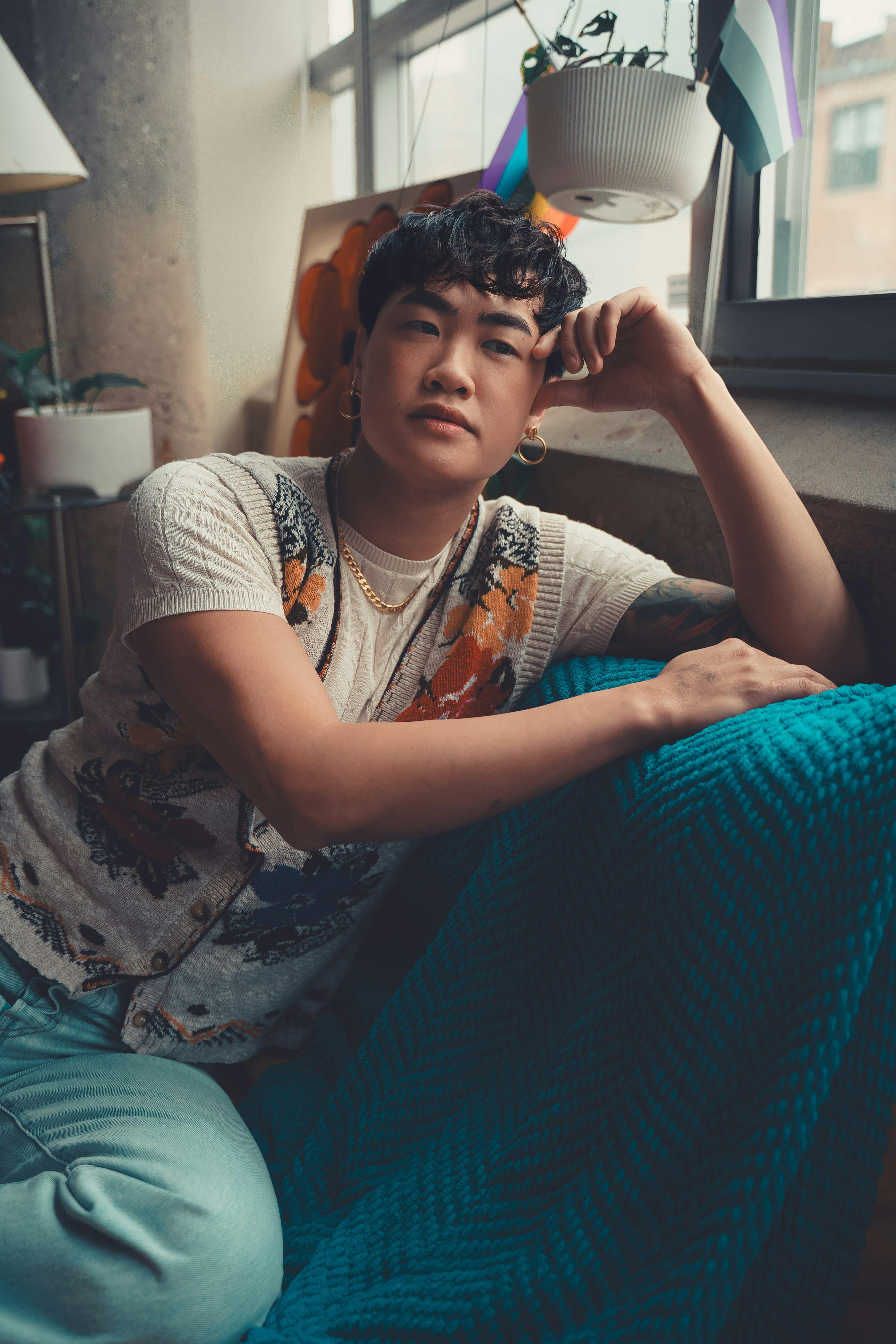 Zadarmo Uvoľnený portrét osoby v štýlovom oblečení sediacej na modrej deke pri okne. Fotka z fotobanky