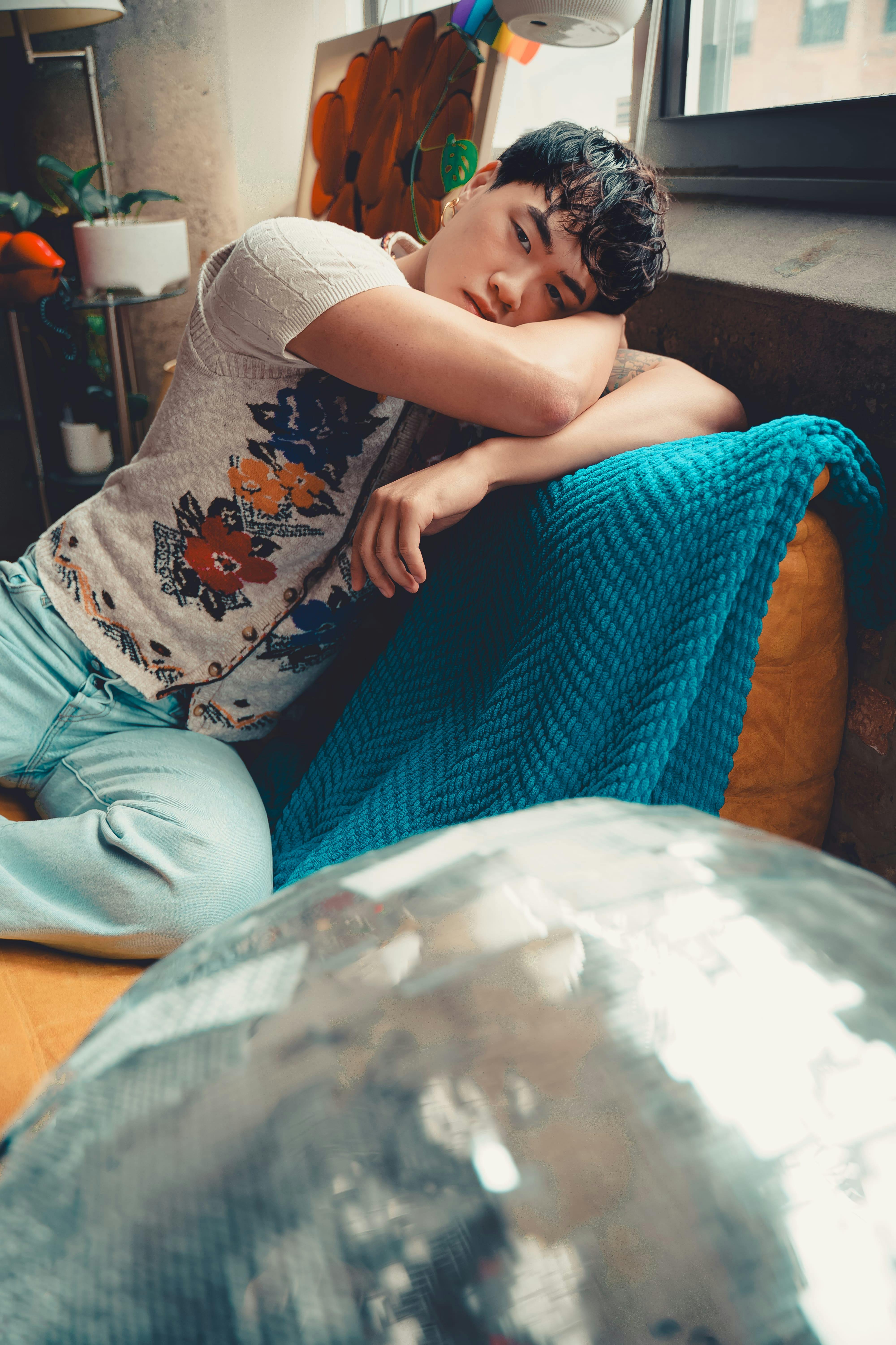 Zadarmo Uvoľnený interiérový portrét muža leňošiaceho na gauči pri okne s farebnou výzdobou. Fotka z fotobanky