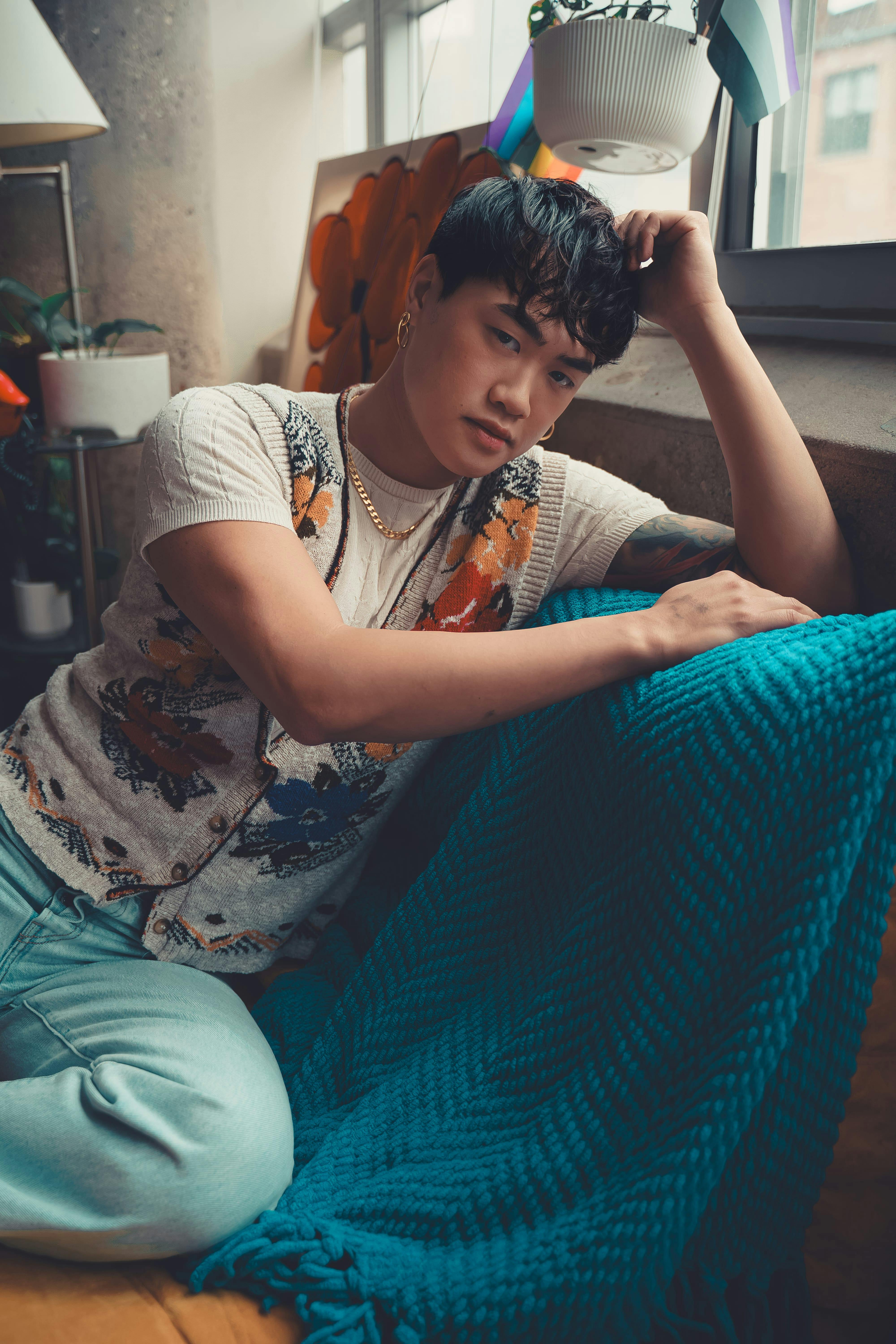 Zadarmo Mladý dospelý sedí zamyslene v interiéri s teplým osvetlením a útulnou výzdobou. Fotka z fotobanky