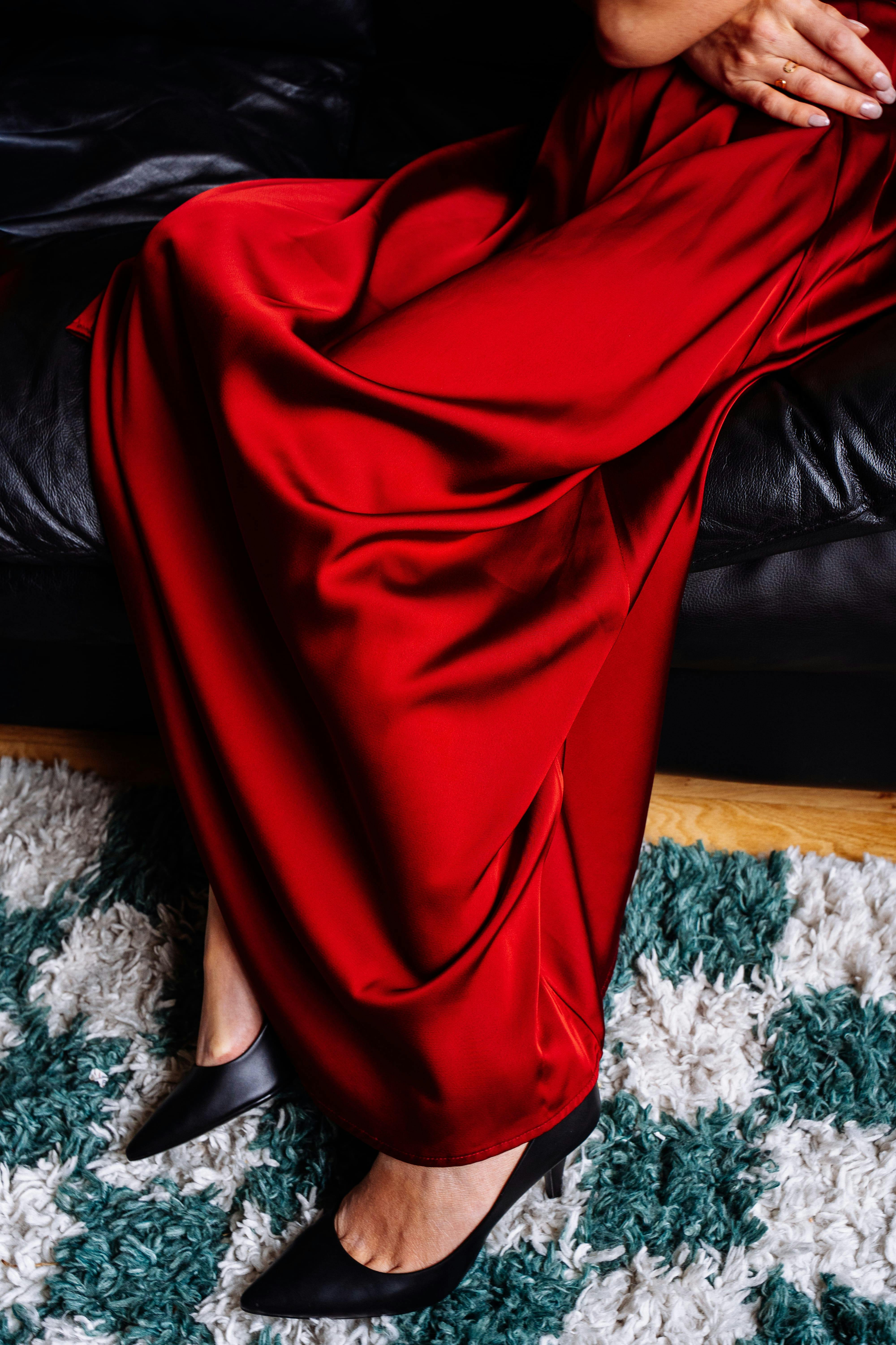 Zadarmo Štýlové červené šaty splývajúce cez pohovku v kombinácii s čiernymi vysokými podpätkami, ktoré predstavujú luxusnú módu. Fotka z fotobanky