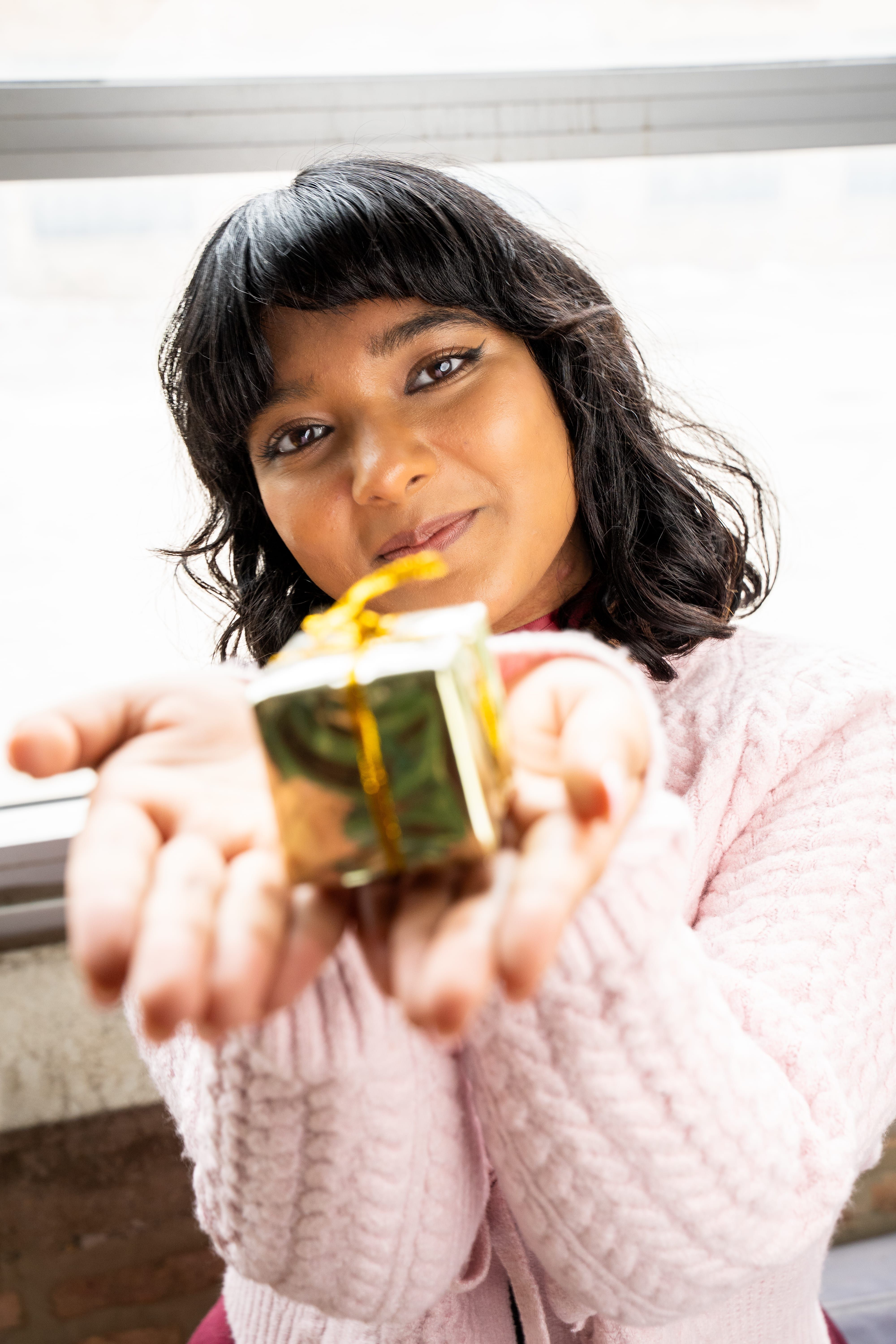 Young Woman Offering a Wrapped Gift Indoors · Free Stock Photo
