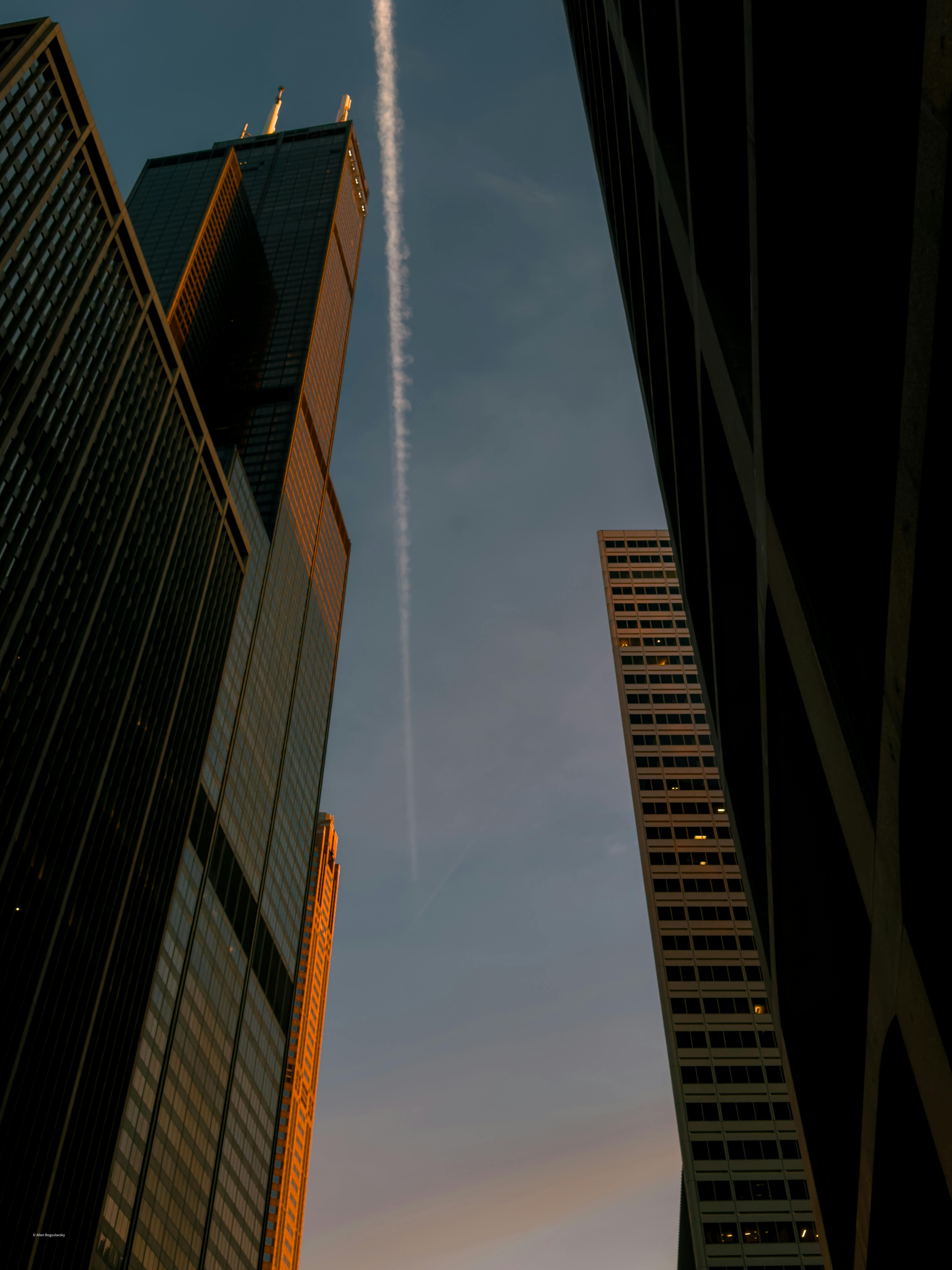 Gratuit Vue de gratte-ciel imposants se détachant sur un ciel de coucher de soleil avec une traînée de condensation, mettant en valeur l'architecture urbaine. Photos
