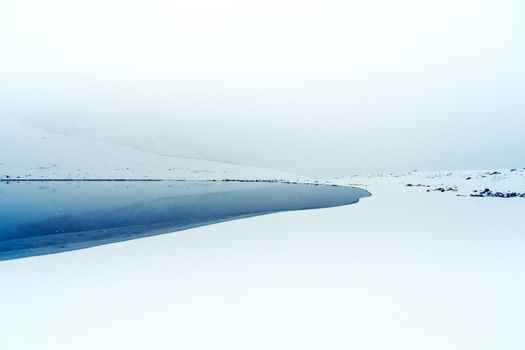 Peaceful snowy landscape with a calm lake under an overcast sky, ideal for winter themes.