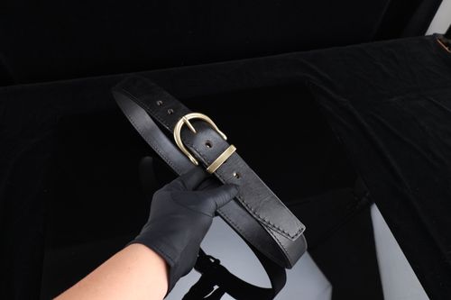 Free Black leather belt with a gold buckle held by a gloved hand on a dark background. Stock Photo
