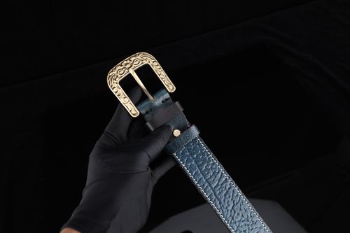 Free Close-up of a blue leather belt with an ornate gold buckle, held in a gloved hand. Stock Photo