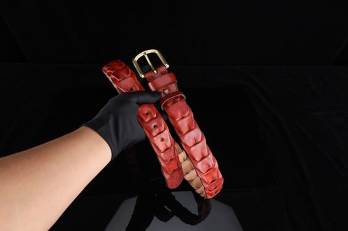 Free A red leather belt with a gold buckle is elegantly held by a gloved hand against a black background. Stock Photo