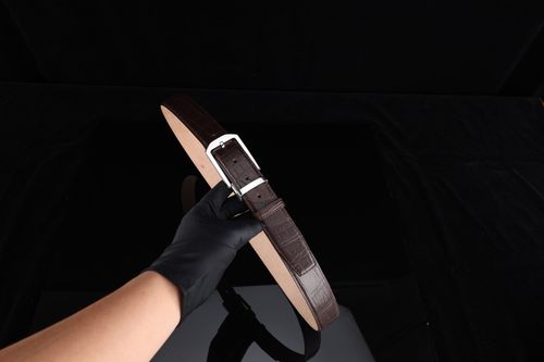 Free Elegant brown leather belt with a silver buckle held on a black background, perfect fashion accessory. Stock Photo
