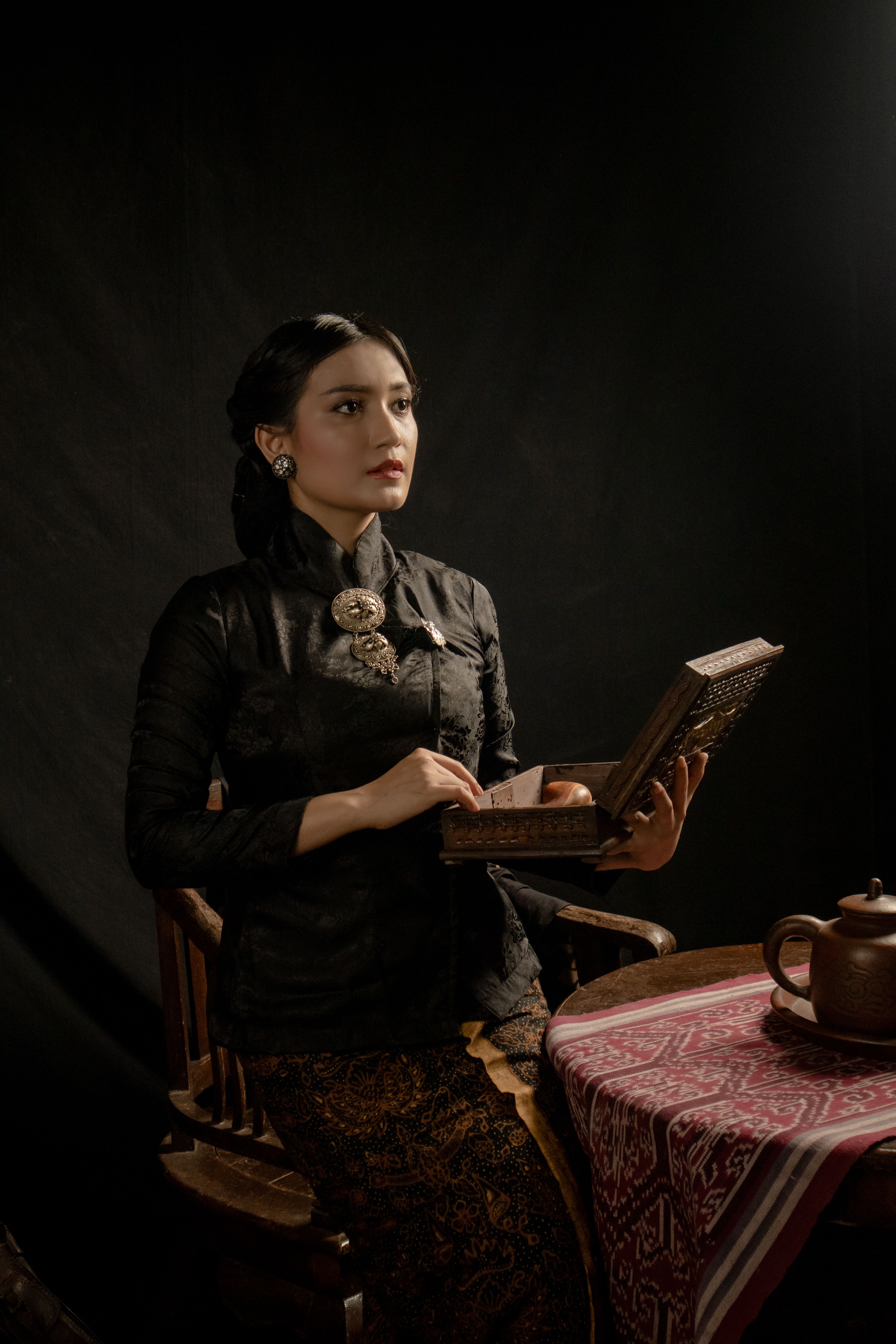 A woman in a traditional Javanese kebaya reads under soft lighting, showcasing cultural heritage.