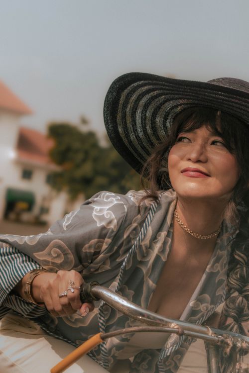Free Smiling woman in wide-brimmed hat riding a bicycle outdoors on a sunny day. Stock Photo