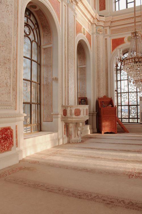 Free Luxurious interior featuring tall arched windows, chandeliers, and intricate ornamentation bathed in sunlight. Stock Photo
