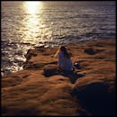 一个女人坐在圣地亚哥的悬崖上，看着日落的海洋