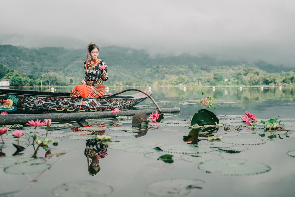 A woman in traditional attire on a boat with lotus flowers in Lake Sebu, Philippines.