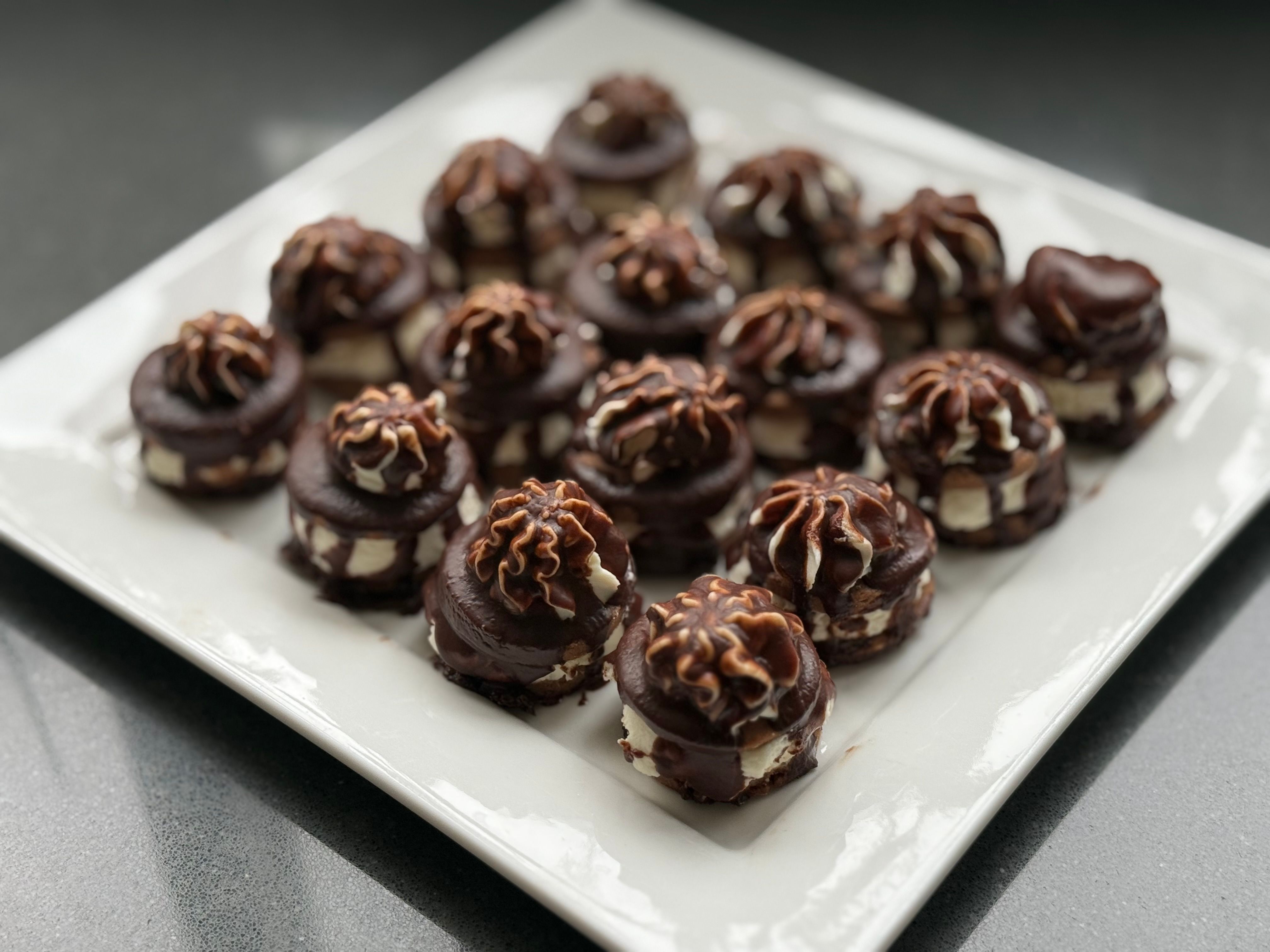 A close-up of mini chocolate ganache desserts artfully arranged on a white plate.
