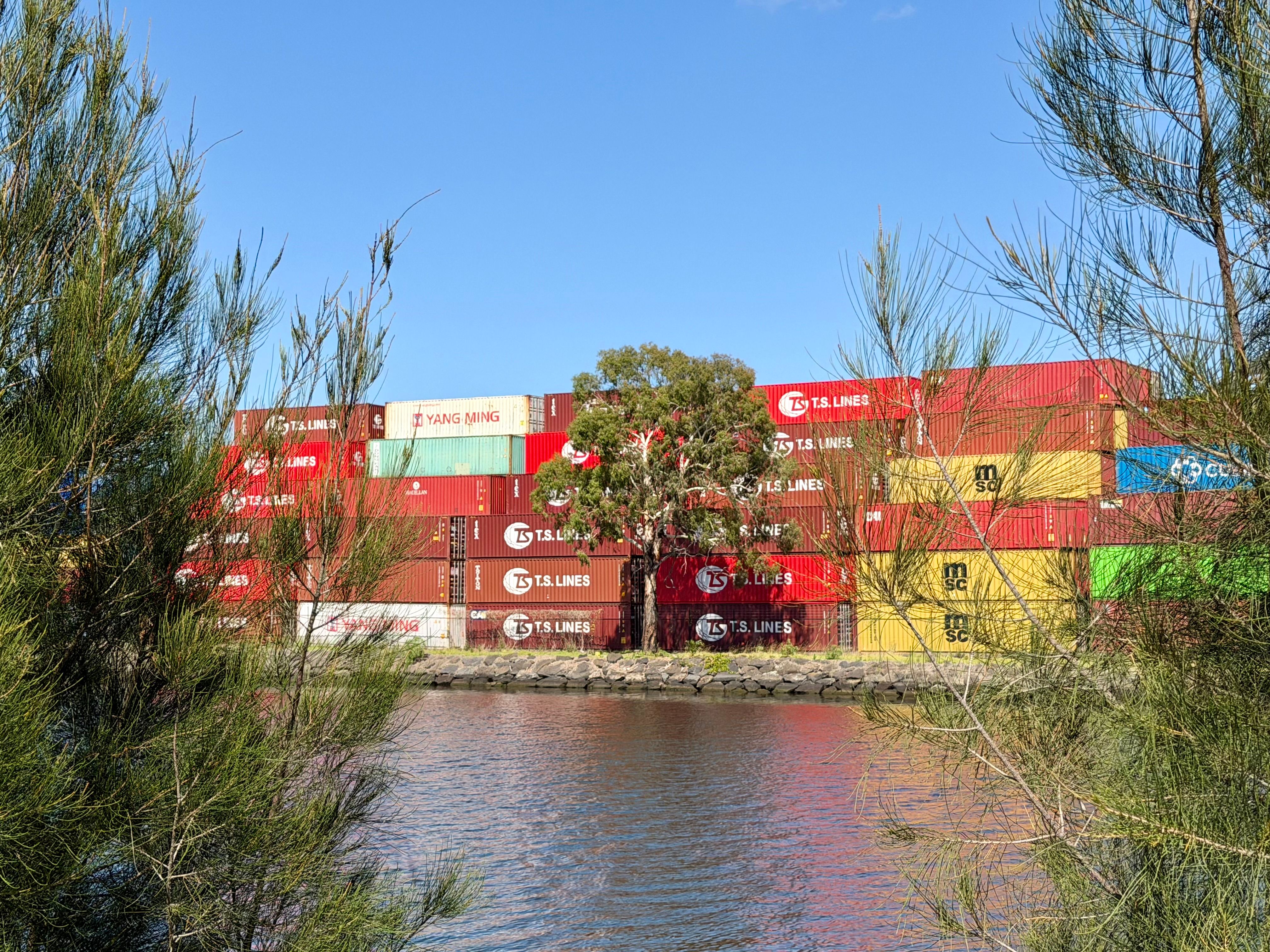 Vibrant shipping containers by a waterside with natural greenery in West Melbourne, Australia.