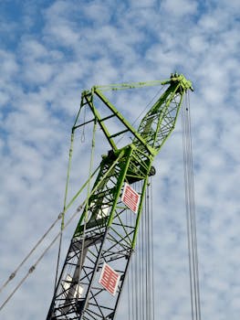 A green crane towering against a cloud-filled sky, showcasing construction industry machinery.