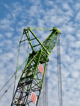 A vibrant green construction crane stands tall against a backdrop of a cloudy sky.