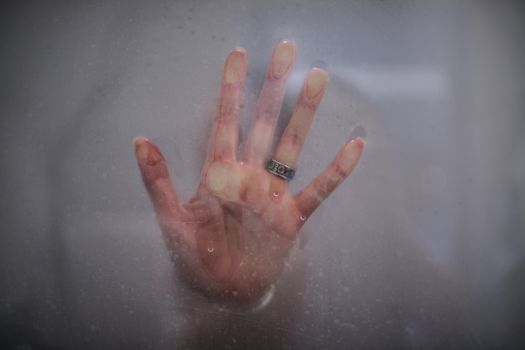 A hand with a ring is pressed against a foggy glass, creating a mysterious and artistic look.