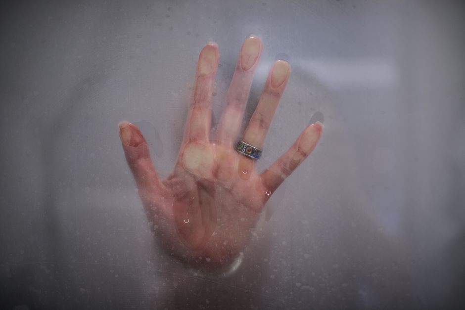A hand with a ring is pressed against a foggy glass, creating a mysterious and artistic look.