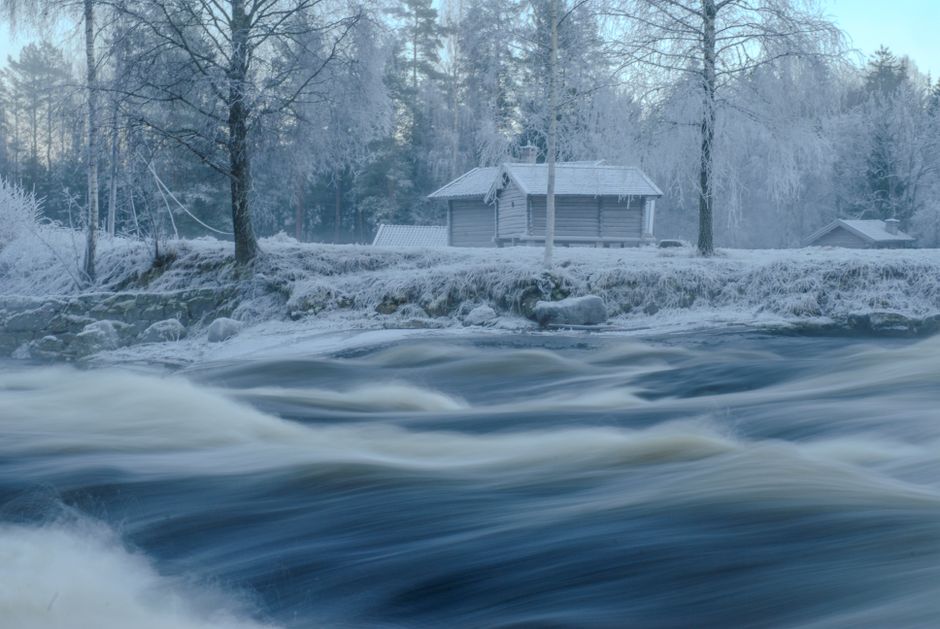 Scenic winter view of a cabin by a swiftly flowing river in Telemark, Norway.