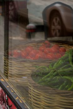 Tomatoes and green peppers reflected in a shop window basket display.
