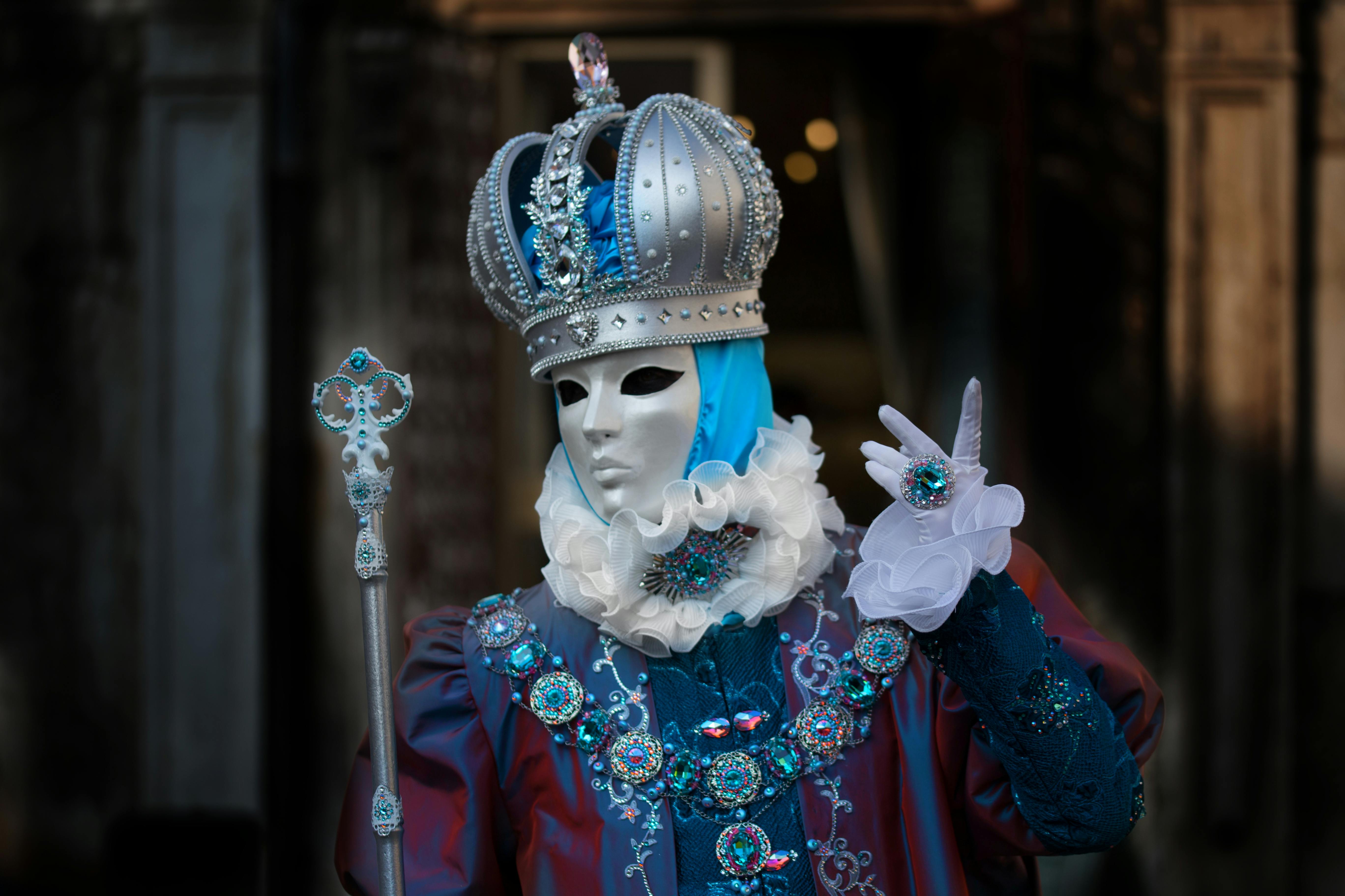 Elaborately dressed figure in royal costume with mask at a carnival event.