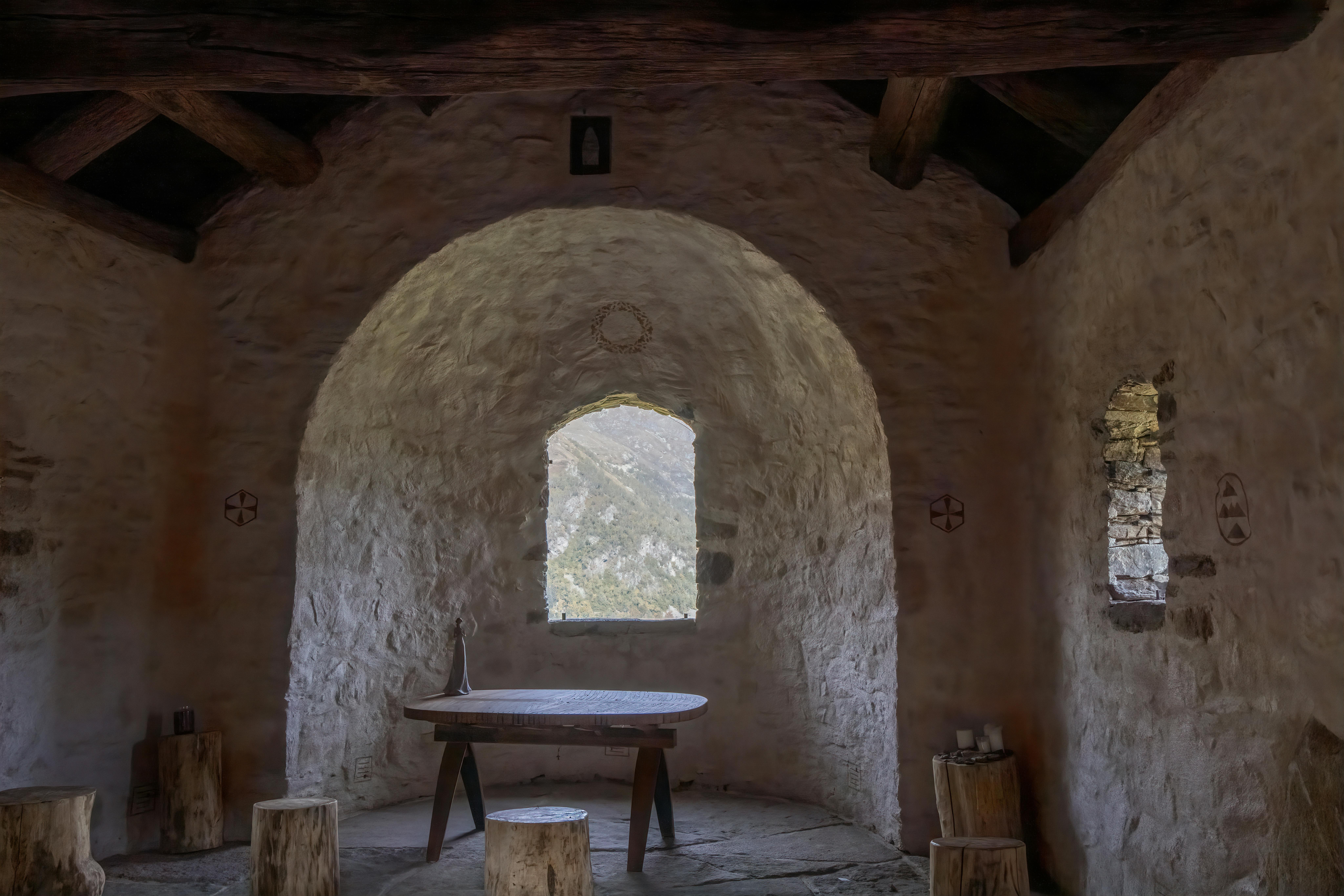 Gratis Habitación rústica con paredes de piedra, mesa y taburetes de madera, que deja entrar la luz natural a través de una ventana arqueada. Foto de stock