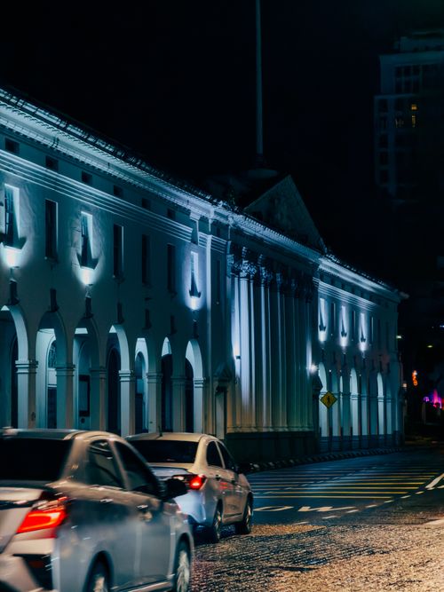 Free Night scene of a lit historic building with passing cars, creating a classic urban atmosphere. Stock Photo