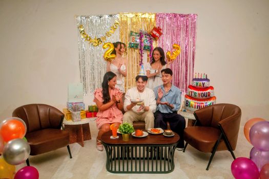 Friends enjoying a lively indoor birthday party with decorations and cake.