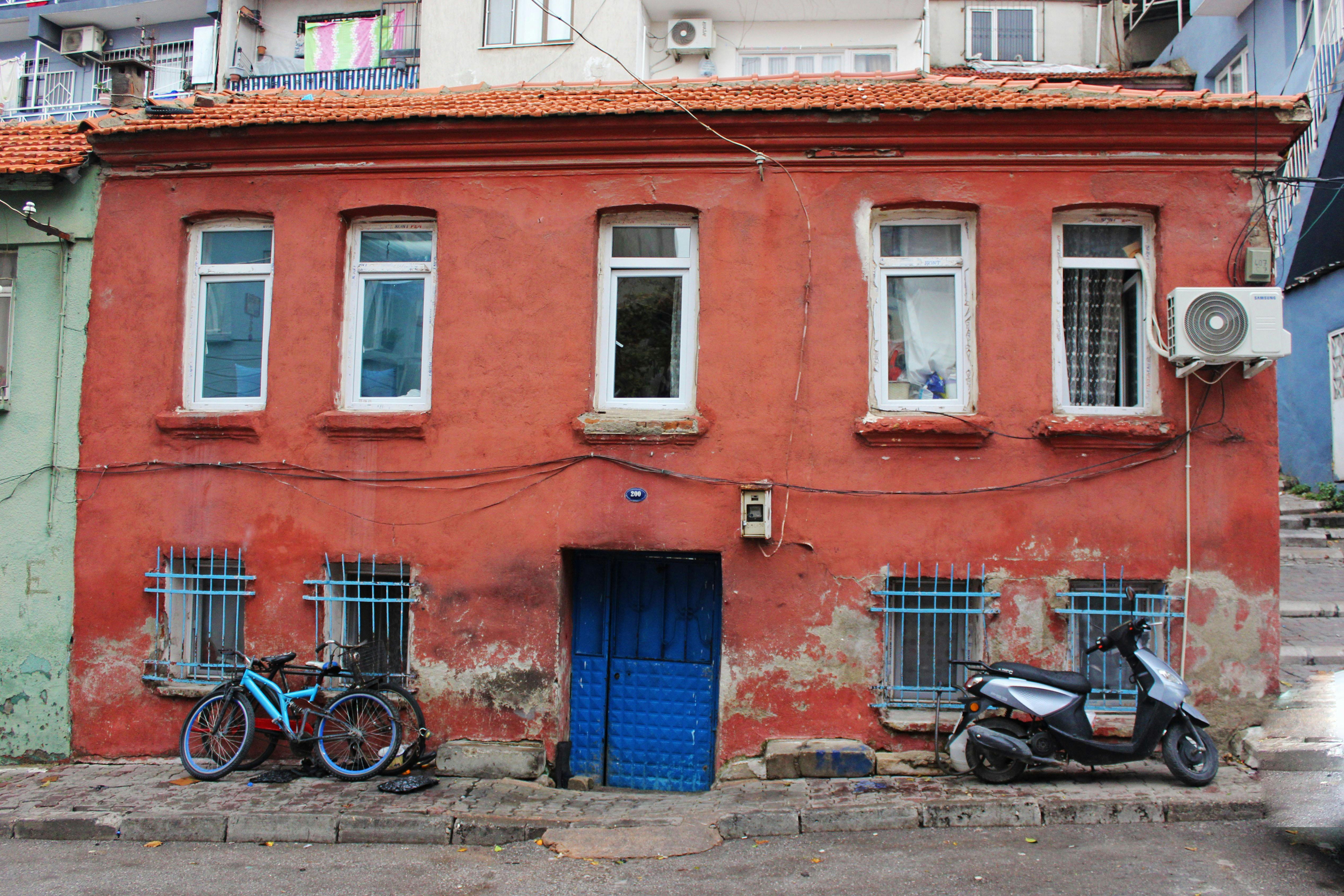 Gratis Una rustica casa rossa con biciclette e un motorino davanti, che mettono in mostra il fascino vintage e il degrado urbano. Foto a disposizione