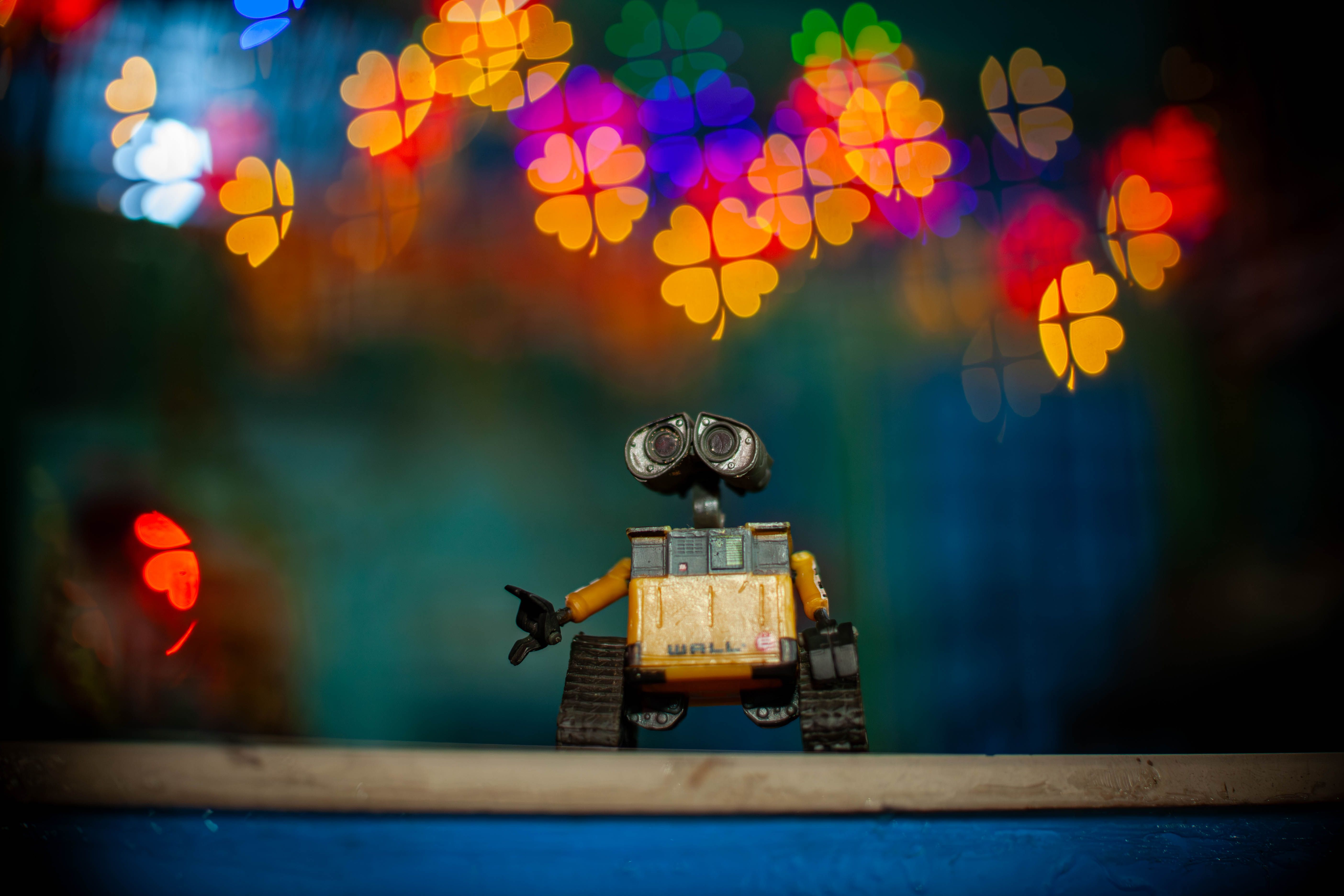Toy Wall-E figure against vibrant heart-shaped bokeh lights background. Creative composition.
