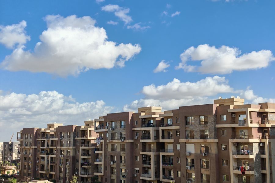 Spacious modern apartment buildings under a bright blue sky with fluffy clouds.