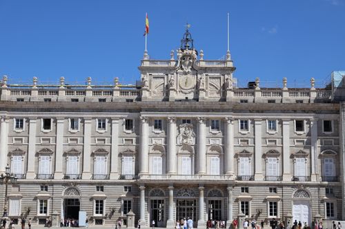 Free Facade of the Royal Palace of Madrid under a bright blue sky with people in front. Stock Photo