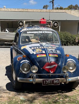 A vintage Volkswagen Beetle adorned with stickers and decorations parked outdoors on a sunny day.