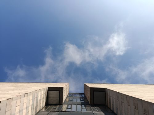 Free Upward view of a modern building contrasting with a clear blue sky and scattered clouds. Stock Photo