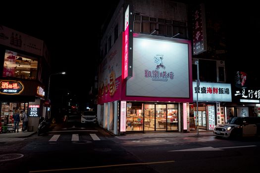 Nighttime streetscape in Taipei with illuminated shops and restaurants, capturing urban life.