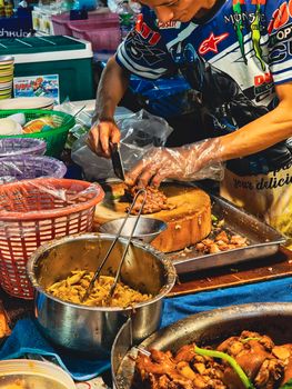 Street vendor skillfully preparing authentic Thai cuisine at a bustling market.