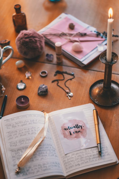 Lit Candle Beside Open Book With Pen